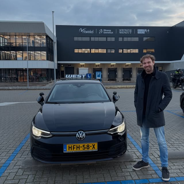 Geslaagde leerling staat trots naast de WEST-lesauto